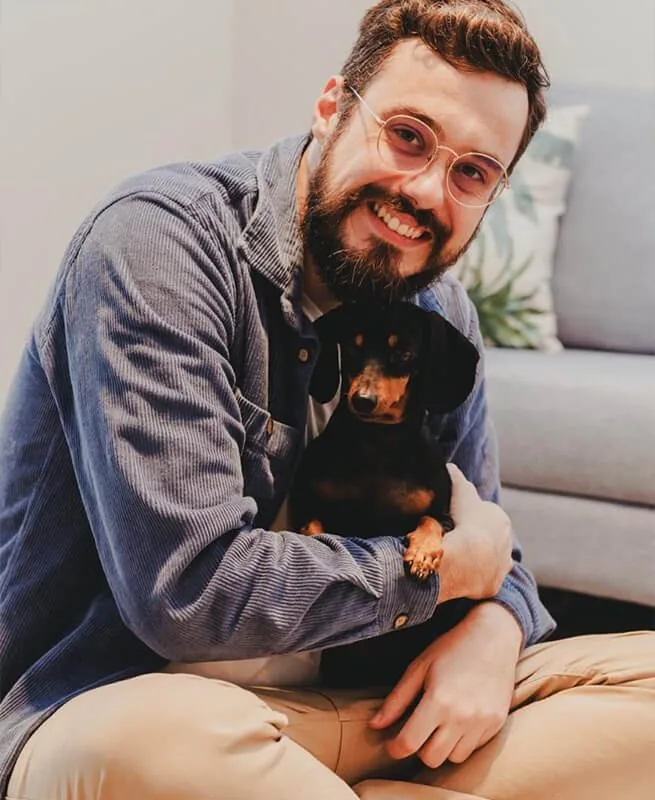 Luan Lovato sentado no chão com sua cachorra Nutella no colo, os dois olhando para a câmera